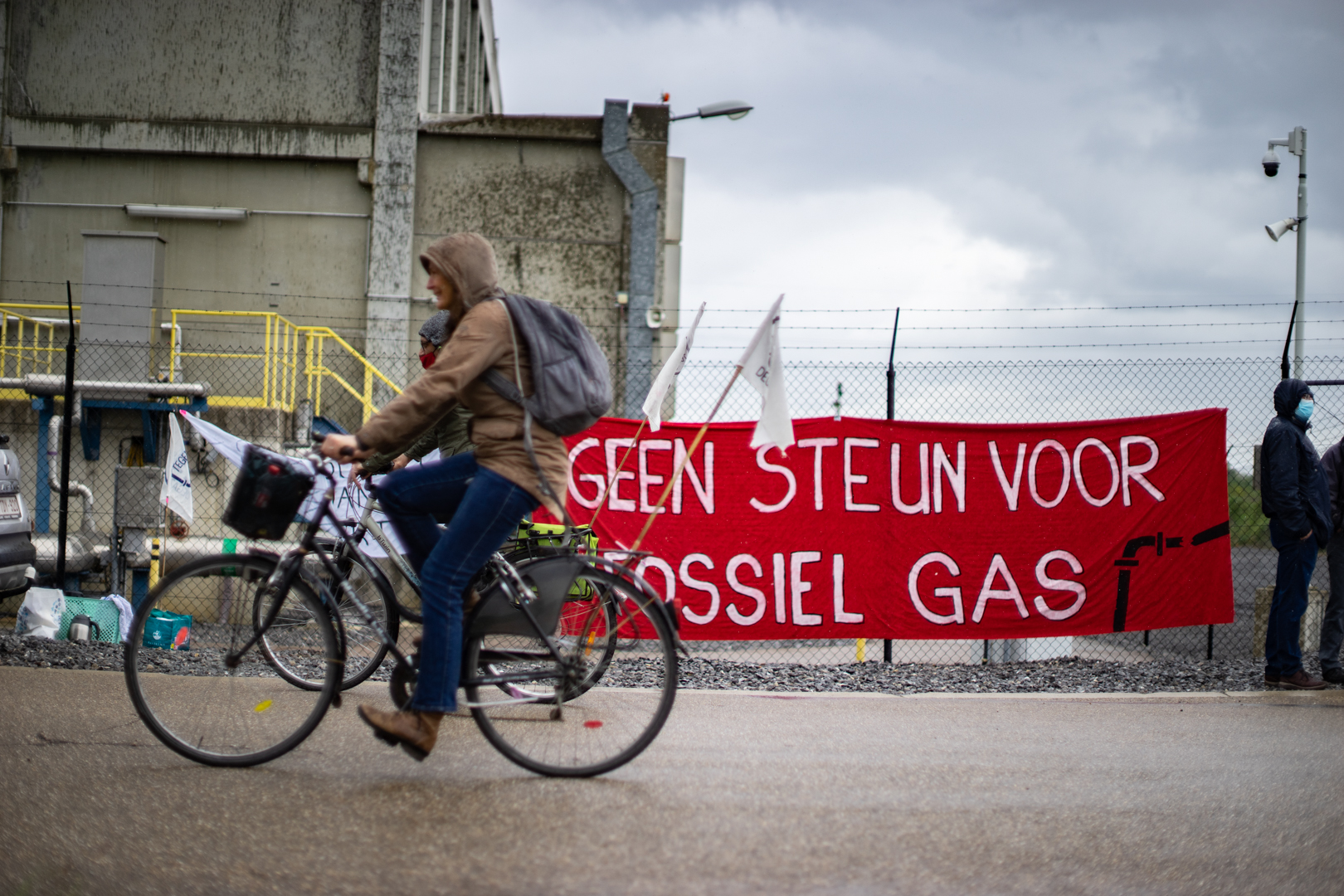 twee fietsers fietsen voorbij een omheining waarop een spandoek hangt "geen steun voor fossiel gas"